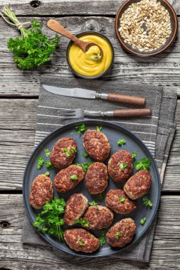 frikadeller, danish meatballs on grey plate on rustic wooden table with mustard and porridge oats, vertical view from above clipart