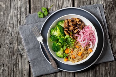 quinoa with sweet potato, sauteed mushrooms, pickled red onion, green peas, boiled broccoli in white bowl on rustic grey table with fork, horizontal view from above, flat lay, free space clipart