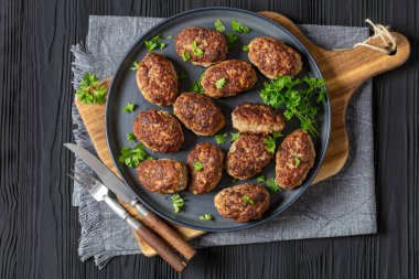 frikadeller, danish meatballs on grey plate on cutting board on black wooden table with fork and knife, horizontal view from above, flat lay, free space clipart