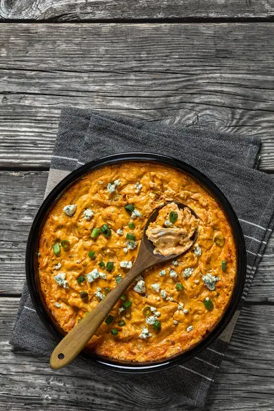 stock image buffalo chicken dip in baking dish with wooden spoon on grey rustic wooden table, vertical view from above, free space