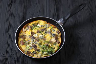 savory omelette with blue cheese, rye croutons and fresh thyme on a skillet on black wooden table, horizontal view from above clipart