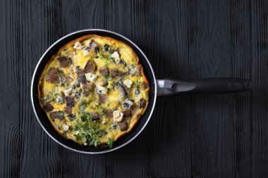 savory omelette with blue cheese, rye croutons and fresh thyme on a skillet on black wooden table, horizontal view from above, flat lay, close-up clipart