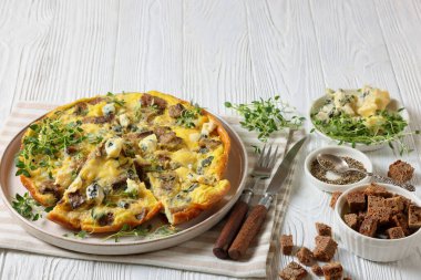 savory omelet with blue cheese, rye croutons and fresh thyme on plate on white wooden table with fork, knife and ingredients, horizontal view from above, free space clipart