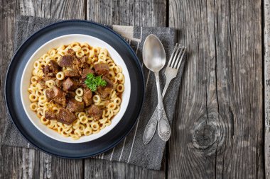 pasta Anelli con carne, pasta rings topped with braised meat in white bowl on grey plate with fork and spoon, horizontal view from above, flat lay, free space clipart