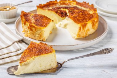 San Sebastian or Basque burnt cheesecake slices on plate and on cake shovel on white wooden table, horizontal  view from above, close-up clipart