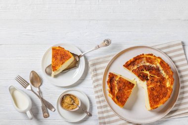 San Sebastian or Basque burnt cheesecake slices on plate and on cake shovel on white wooden table with brown sugar and cream, horizontal view from above, flat lay, free space clipart