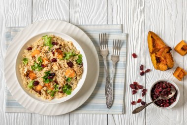 warm quinoa pumpkin salad with dried cranberries, walnuts  and fresh lettuce in white bowl on white wooden table with ingredients and forks, horizontal view from above,  flat lay clipart