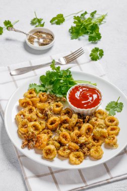 deep fried battered baby squid rings and tentacles with cilantro and tomato sauce on white plate on white concrete table, vertical view from above, close-up clipart