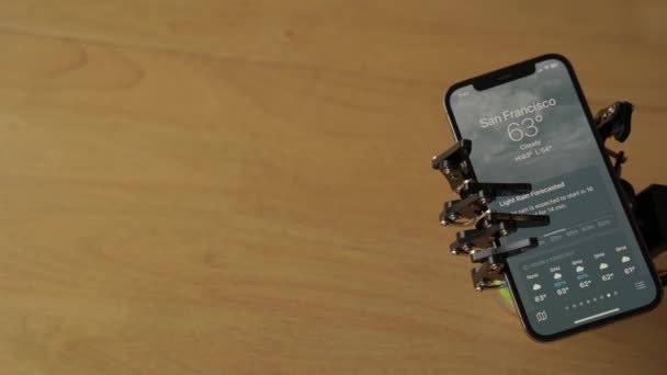 Mão Robótica Segurando Iphone Com Aplicativo Tempo Aberto Exibindo Tempo — Vídeo de Stock
