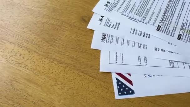 木製のテーブルに広がる米国の税形態のトップダウンビューは 部分的に見えるアメリカの国旗で外れました — ストック動画