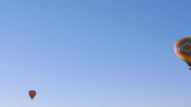 İki sıcak hava balonunun, berrak ve geniş bir mavi gökyüzüne uzanan uzak bir görüntüsü.