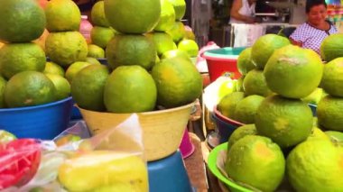 Canlı yeşil limon yığınları, arka planda gülümseyen bir satıcı ile yerel bir pazarda sergileniyor, taze ürün alışverişinin özünü yakalıyor.