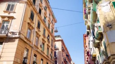 Geleneksel Napoli binaları dar bir cadde boyunca uzanır, balkonları açık mavi gökyüzünün altında asılı çamaşırlarla süslenir..