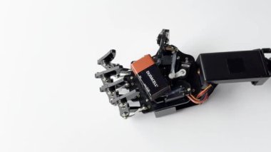 Robotik bir el, Bataryayı beyaz bir arkaplana karşı kavrıyor. Gelişmiş robotik teknolojinin hassasiyetini ve maharetini sergiliyor.