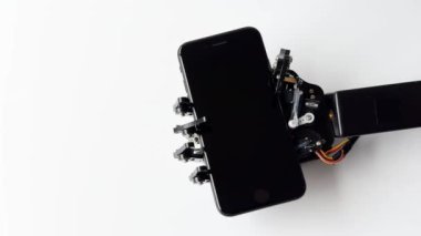 Robotik bir el akıllı telefonu beyaz bir arkaplanda tutar, ileri teknoloji ve robot teknolojisinin hassasiyetini ön plana çıkarır..