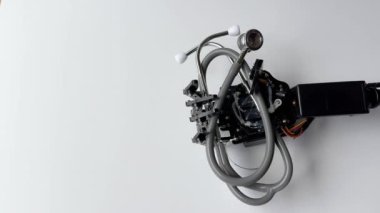 Robot bir el steteskopu beyaz arka plana doğru tutar. Çekim, modern robotik teknolojinin çok yönlülüğünü ve hassasiyetini gösteriyor..