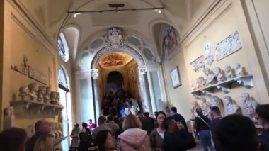 Turistler Vatikan Müzesi 'nin zengin dekore edilmiş bir koridorunu klasik büstler ve başka bir galeriye uzanan ayrıntılı kemerlerle dolduruyorlar. Sahne, sanat ve mimarinin karışımını yakalar..