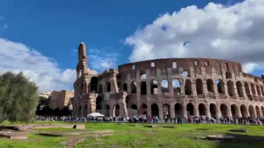 Roma 'daki Kolezyum' un Roma Forumu 'ndan bir görüntüsü, antik yapının belirgin bir şekilde bulutlu bir gökyüzünün zeminine karşı durduğu. Sahne, bu ikonik simgelerin ihtişamını ve tarihsel önemini yakalıyor..
