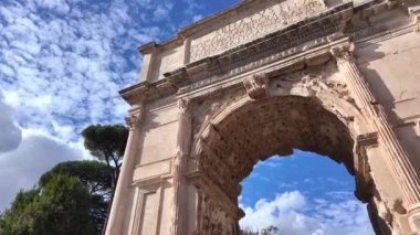 Titus 'un kemeri Roma' da, parlak mavi bir gökyüzünün altında, dağınık bulutlarla görkemli bir şekilde duruyor. Bu ikonik antik yapı Roma mühendisliği ve tarihsel ihtişamın bir kanıtıdır..