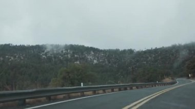 Büyük Kanyon Güney Rim otoyolunda sis kaplı dağlar ve sık ormanlarla çevrili sisli, dolambaçlı bir yol. Sahne, bu ikonik bölgede sürüşün gizemli ve sakin atmosferini yakalıyor..