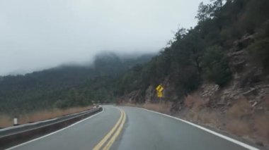 Otoyol AZ-89A sislerle kaplı dağların arasından esiyor ve son yağmurdan dolayı yol ıslanıyor. Sahne, bu Arizona otoyolunun engebeli ve atmosferik güzelliğini gösteriyor..