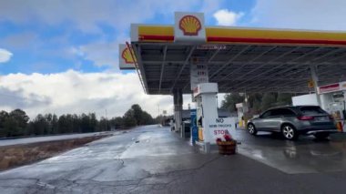 Yağmurlu bir günde yağmurlu bir kaldırım ve bulutlu bir gökyüzü ile yakalanan AZ-89A karayolu boyunca bir Shell benzin istasyonu. Olay yeri, park halindeki bir arabanın ağaçların ve açık yolların önünde yakıt ikmali yaptığını gösteriyor..