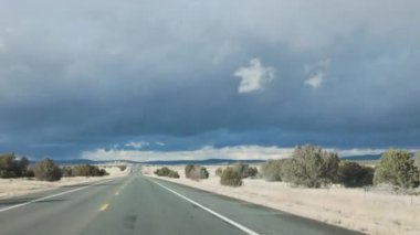 AZ-89A karayolunun açık bir alanı fırtınalı bir gökyüzünün altında, yol üzerinde kara bulutlar belirdi. Sahne, Arizona 'nın dramatik havasını ve uçsuz bucaksız manzarasını çekiyor..