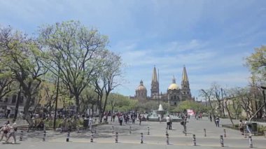 Görkemli Guadalajara Katedrali Plaza de la Liberacin 'de berrak mavi gökyüzünün altında ziyaretçiler ve ağaçlarla çevrili duruyor. Bu sembolik simge, şehrin zengin tarihi ve kültürünün bir sembolüdür..