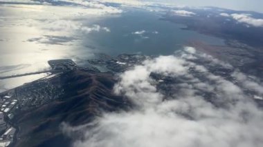 Arka planda okyanus olan bir kıyı şehrinin havadan görünüşü. Kıyı şeridi, binalar ve yuvarlanan tepeler bulutların altında görülebilir..