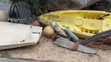 Kıyıda eski, yıpranmış kano ve şamandıra koleksiyonu var. Parlak renkli ekipmanlar kırsal ve yıpranmış çevreyle çelişiyor ve kıyı yaşamına kısa bir bakış sunuyor..
