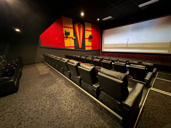 modern movie theater with reclined leather seating and a large screen showing a preview. The room is empty, highlighting its sleek design and the quiet atmosphere before the show.