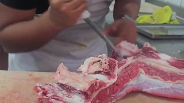 Guadalajara, Jalisco, Meksika; 12.12.24: Bir kasap bir pazarda taze eti kesin kesikler kullanarak doğruyor. Kırmızı et, beyaz önlük ve kesme tahtası taze yiyecek hazırlama sürecinin ham halini gösteriyor..