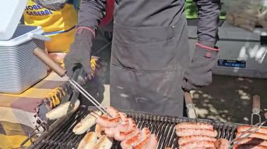Siyah eldivenli ve önlüklü bir satıcı Chapala 'da mangal yapmak için çiğ sosisleri dikkatlice şişliyor. Sosisler ızgarada cızırdarken dumanlı barbekü kokuları havayı dolduruyor..