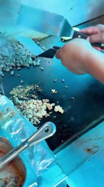 Bir satıcı, taco hazırlığı sırasında paslanmaz çelik bir tako standında sıcak, düz bir ızgarada tortilla üzerine doğranmış et ekler..