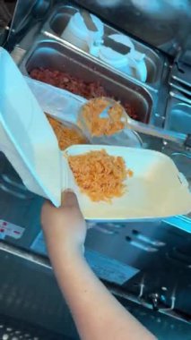 Bir satıcı, taco, pirinç ve fasulye kepçesini bir tako standında köpüklü yemek kabına koyar..