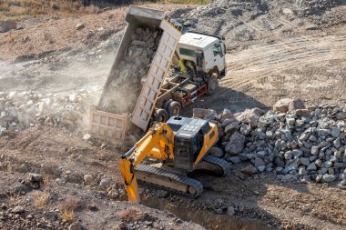 White color excavation dump truck is unloading to rocks in the construction site.