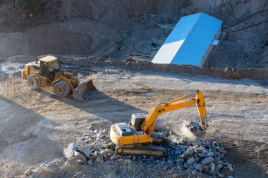 Yellow color excavator is loading some rocks to red color earth dump truck in the construction site.