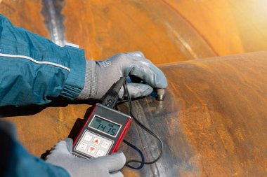 Inspector is measuring thickness of the pipe material from near to weld with a portable ultrasonic wall thickness measurement gauge. It is a method of performing non destructive measurement (gauging).