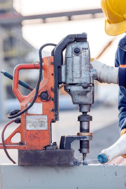 Worker is making a hole in the steel structure material with portable magnetic drill machine in the construction site. It can use twist drill bits, annular cutters and milling cutters.
