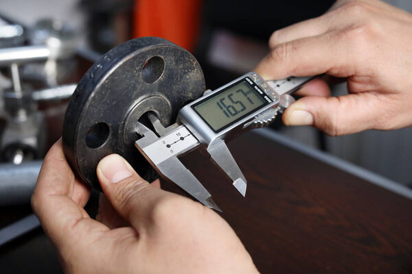 The worker is measuring to inner diameter of flange with vernier caliper gauge. Vernier calipers are widely used in scientific laboratories and in manufacturing for quality control measurements.