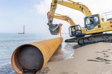 Excavators are carrying pile pipe to sea. Pipe piles are either a welded or seamless steel pipe which may be driven either open-ended or closed-ended. It is easy to understand type of piling.