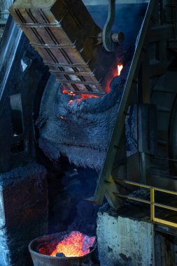 Arkasında ateş olan büyük metal bir fırın. Eriyen metal endüstriyel dökümhanedeki büyük eritme kabına dökülüyor. Metaller, onları eritip sıvıya dönüştürerek, metali kalıba döküyorlar..