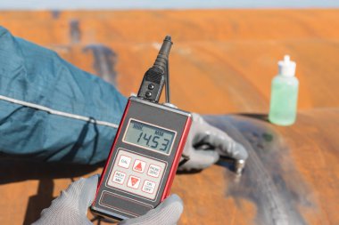 Inspector is measuring thickness of the pipe material from near to weld with a portable ultrasonic wall thickness measurement gauge. It is a method of performing non destructive measurement (gauging).