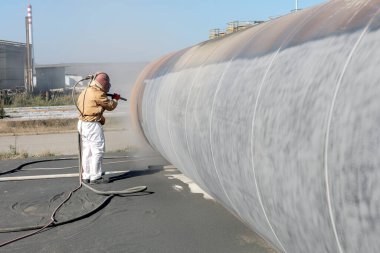 The sandblaster is sanding to steel pipe material. Abrasive blasting, more commonly known as sandblasting, is the operation of forcibly propelling a stream of abrasive material against a surface.