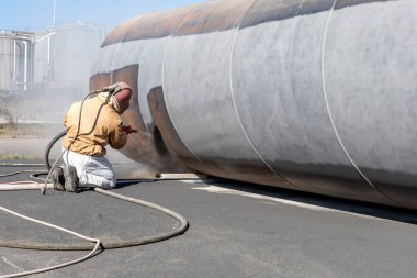 The sandblaster is sanding to steel pipe material. Abrasive blasting, more commonly known as sandblasting, is the operation of forcibly propelling a stream of abrasive material against a surface .