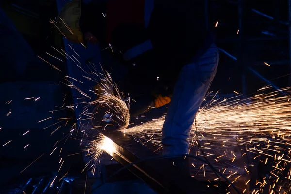 Industrial worker cutting metal with angle grinder in a factory. The worker is cutting a steel material with a grinding machine in the construction site.