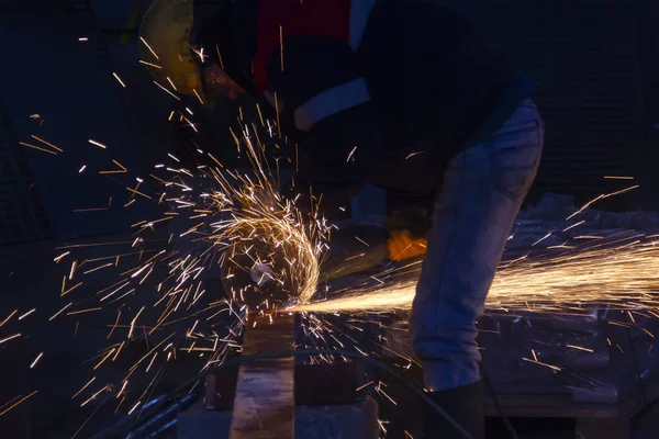 Industrial worker cutting metal with angle grinder in a factory. The worker is cutting a steel material with a grinding machine in the construction site.