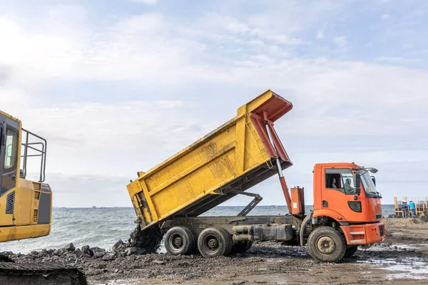 Dump truck unloading soil at the construction site. Earthmoving. The dump truck is unloading to excavation to sea for filling and an excavator.