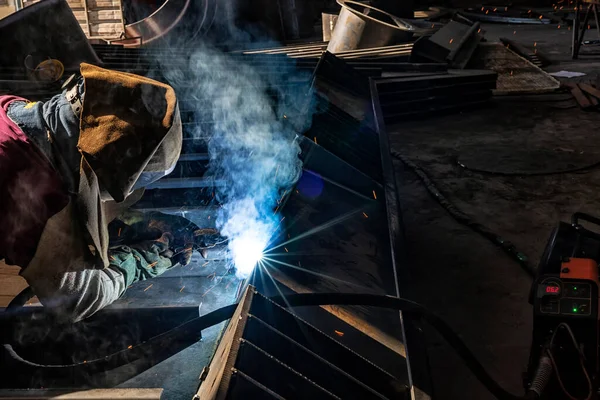 The welder is welding a structural steel with gas metal arc welding ( GMAW ) in the workshop. Welder welding metal with sparks in workshop
