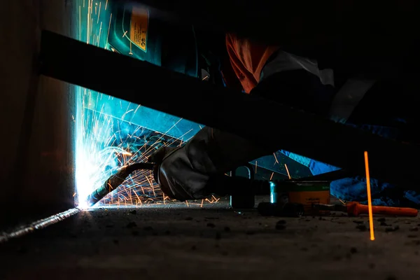 The welder is welding a structural steel with gas metal arc welding ( GMAW ) in the workshop.